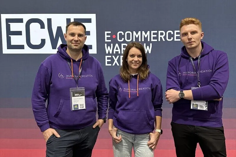 Trzy osoby z Aurora Creation w firmowych bluzach przed ścianką konferencji E‑Commerce Warsaw Expo.
